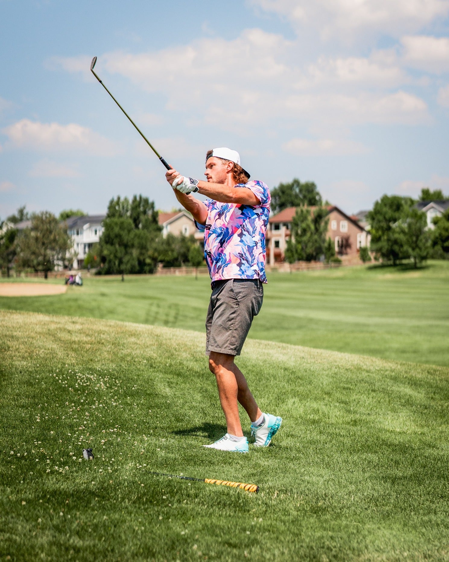 A golfer in a vibrant melting floral shirt swings a club on a sunny course, showcasing bold golf fashion.