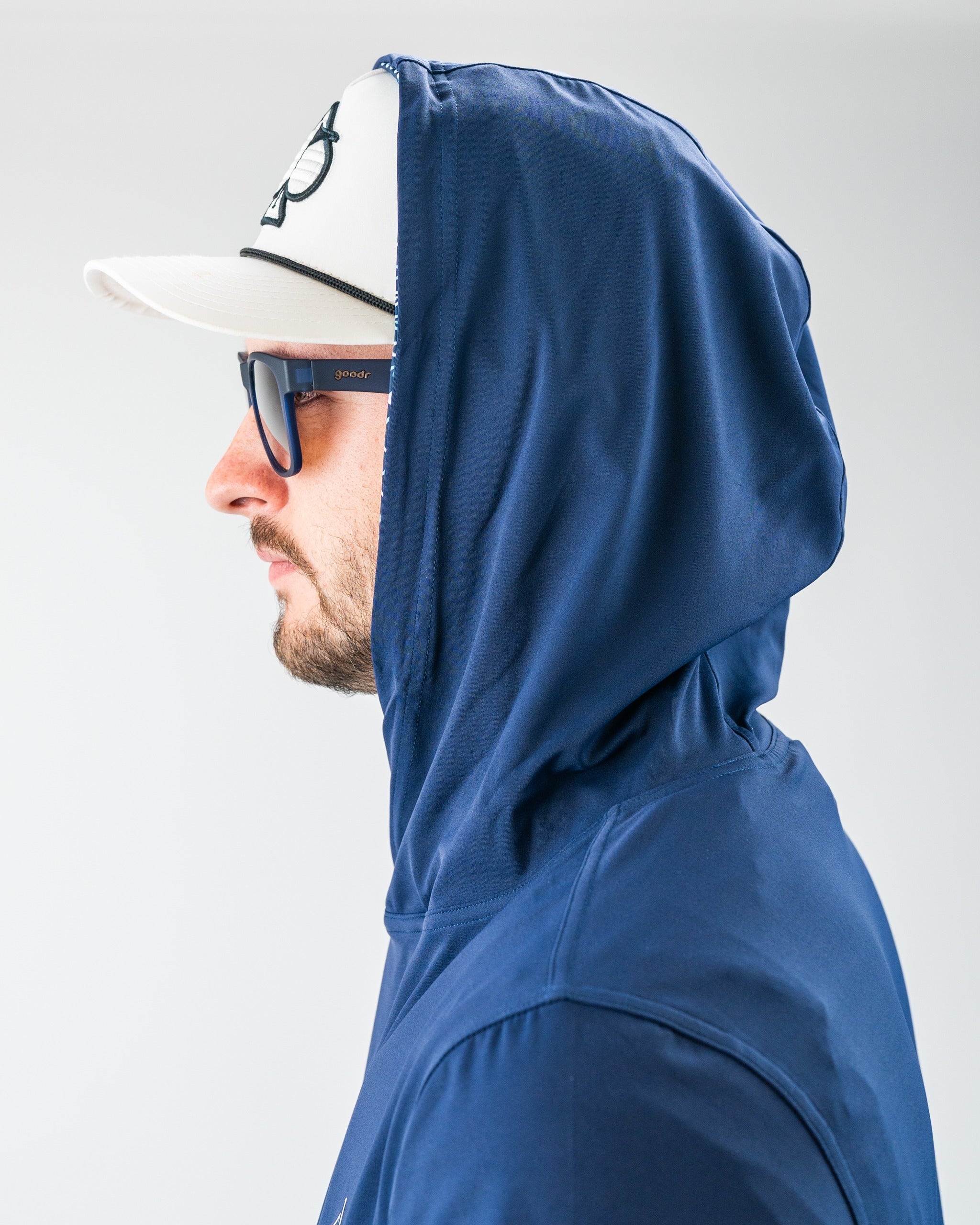 Man wearing a navy blue hooded golf jacket, white cap, and blue sunglasses, showcasing bold golf apparel for standing out ...