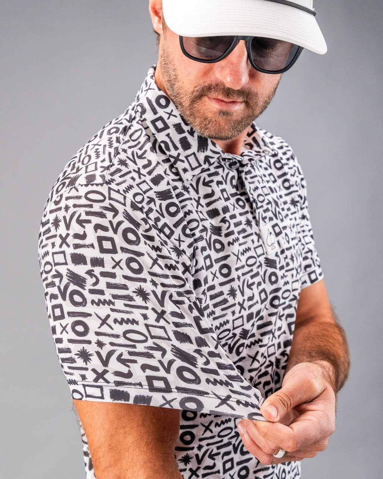 Close-up of a man wearing a bold black-and-white patterned golf shirt with geometric shapes, paired with dark sunglasses a...