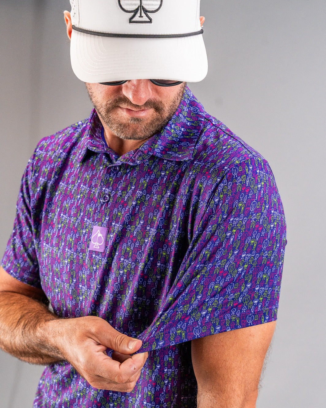 Man wearing a vibrant purple golf shirt with multicolored abstract patterns, featuring a small spade logo.