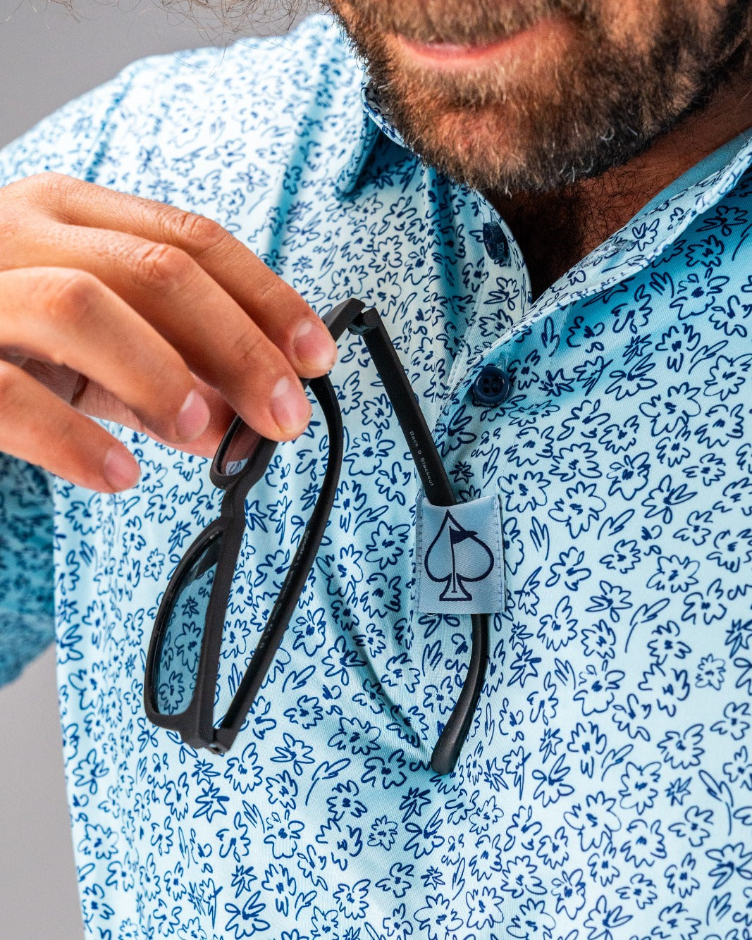 A man holds a black golf accessory against a blue floral patterned shirt, showcasing a unique design.