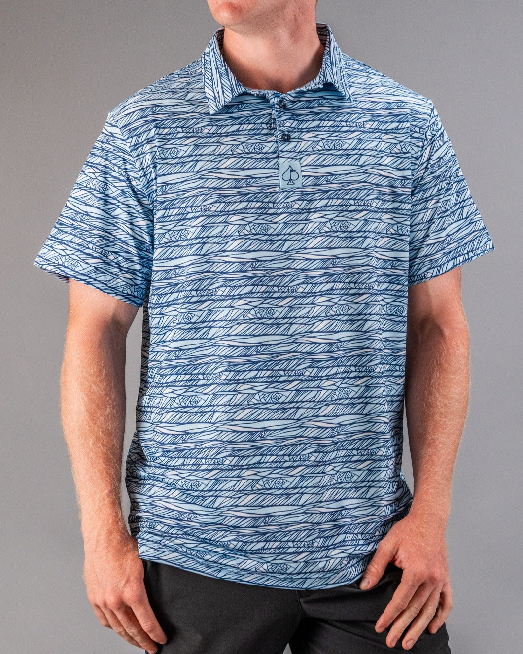 Bright blue golf polo with a bold, abstract line and leaf pattern, featuring a small spade logo on the chest.