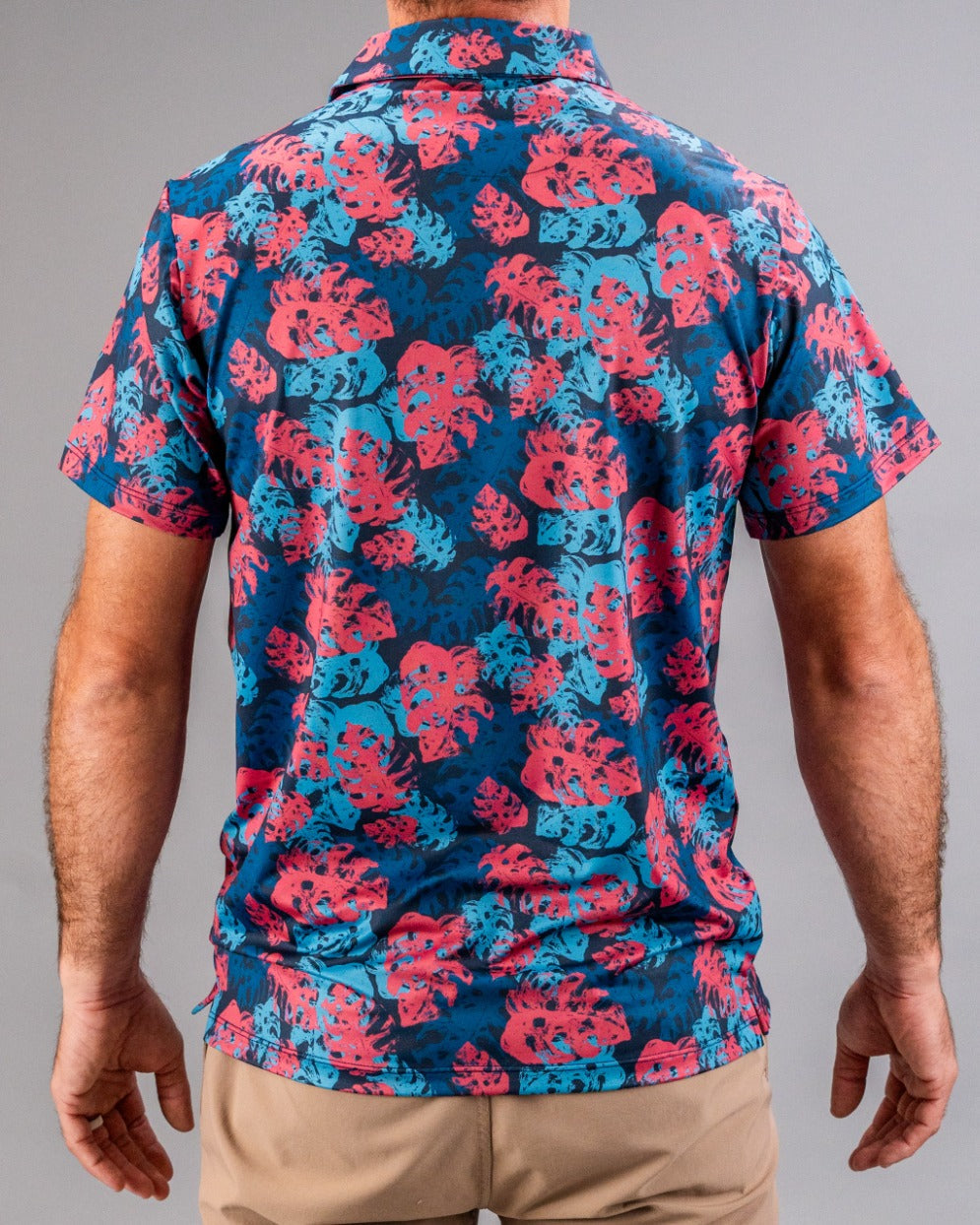 Vibrant men's short-sleeve button-up shirt with pink and blue tropical leaf pattern, perfect for bold golf style.