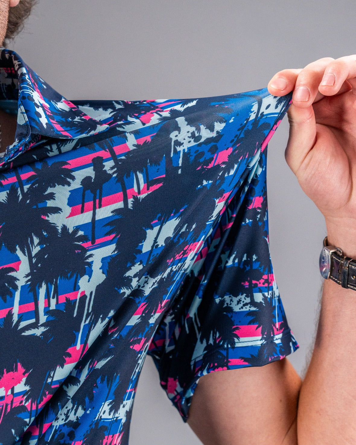 Close-up of a colorful golf shirt with a bold pink, blue, and black palm tree pattern, showcasing unique golf apparel for ...