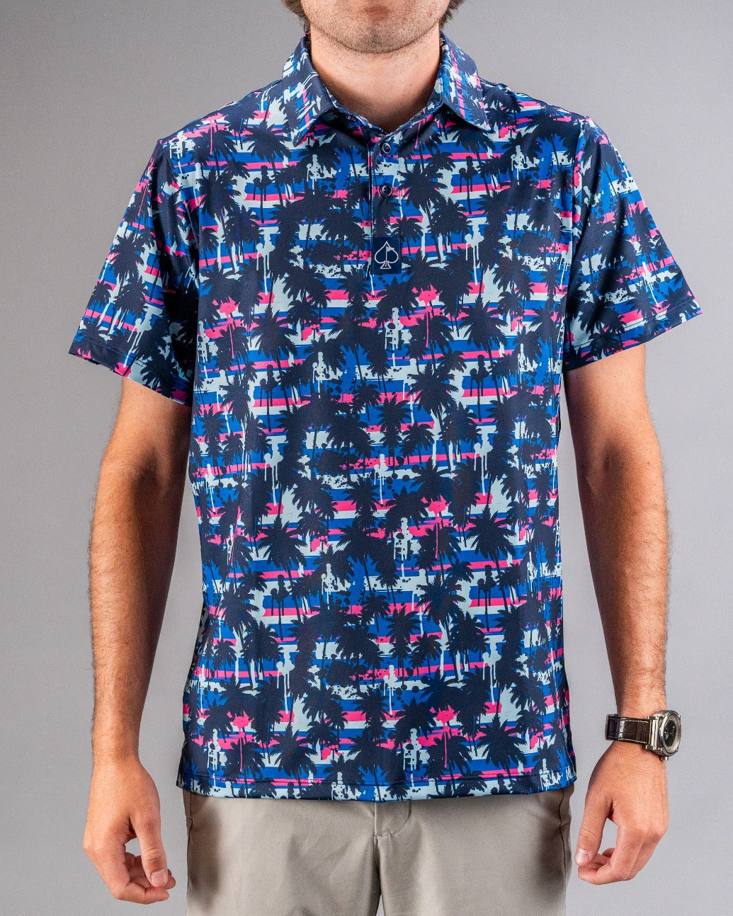 Men's tropical print golf polo with navy, pink, and blue palm trees and stripes, perfect for bold on-course style.