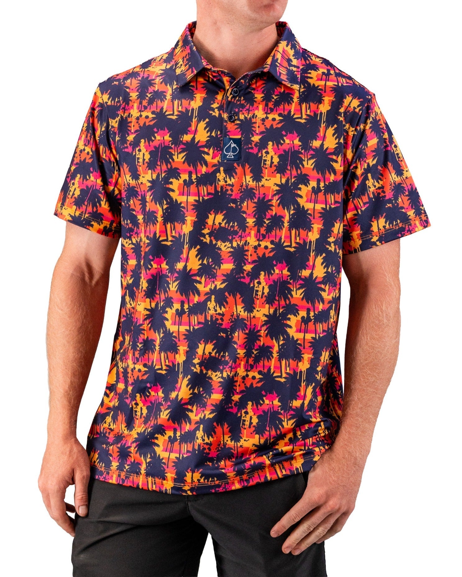 Bright tropical print golf polo with navy palm trees, pink, orange, and yellow sunset background, short sleeves, and class...