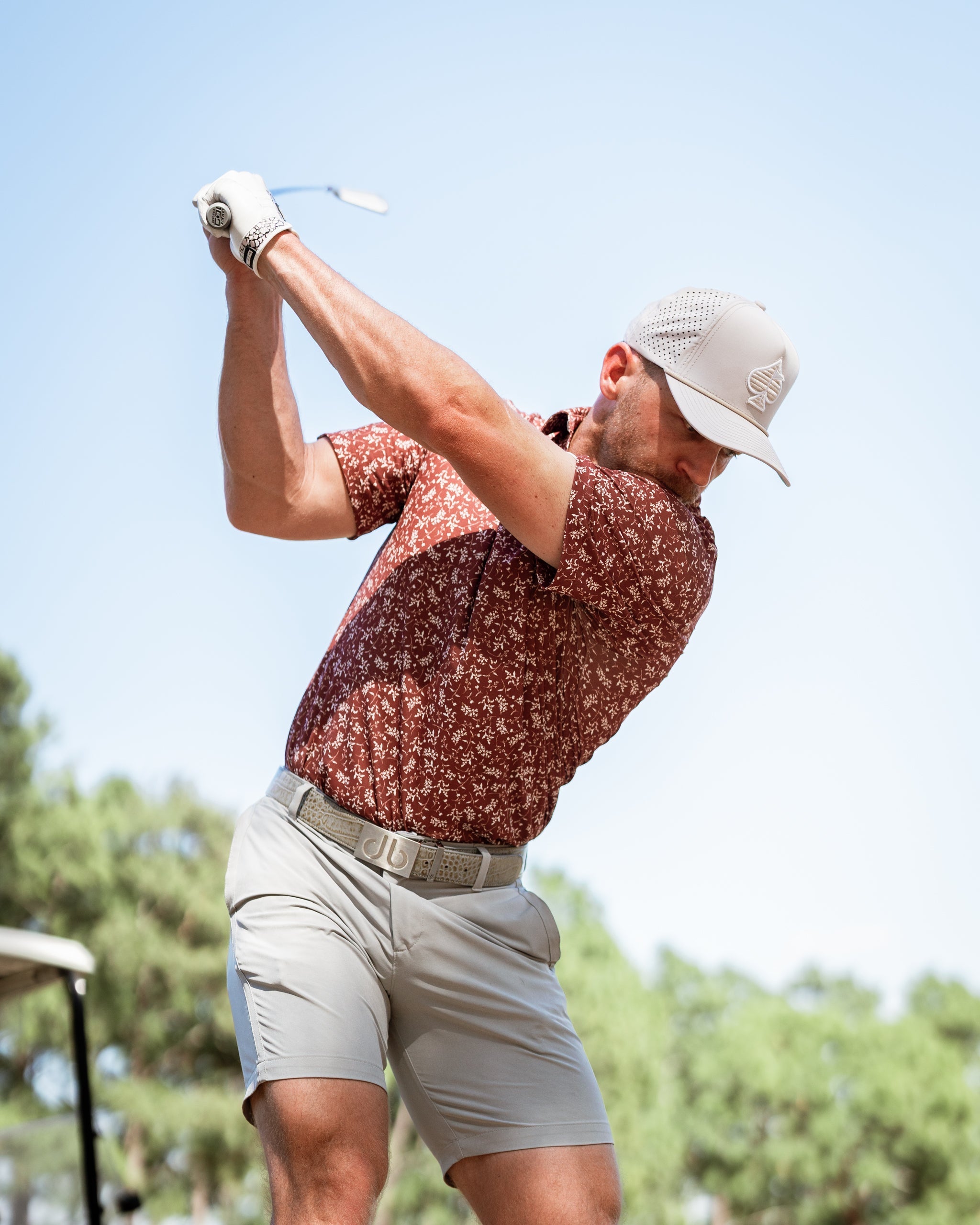 A golfer swings a club while wearing a floral-patterned shirt and a light cap, showcasing bold autumn colors on the course.