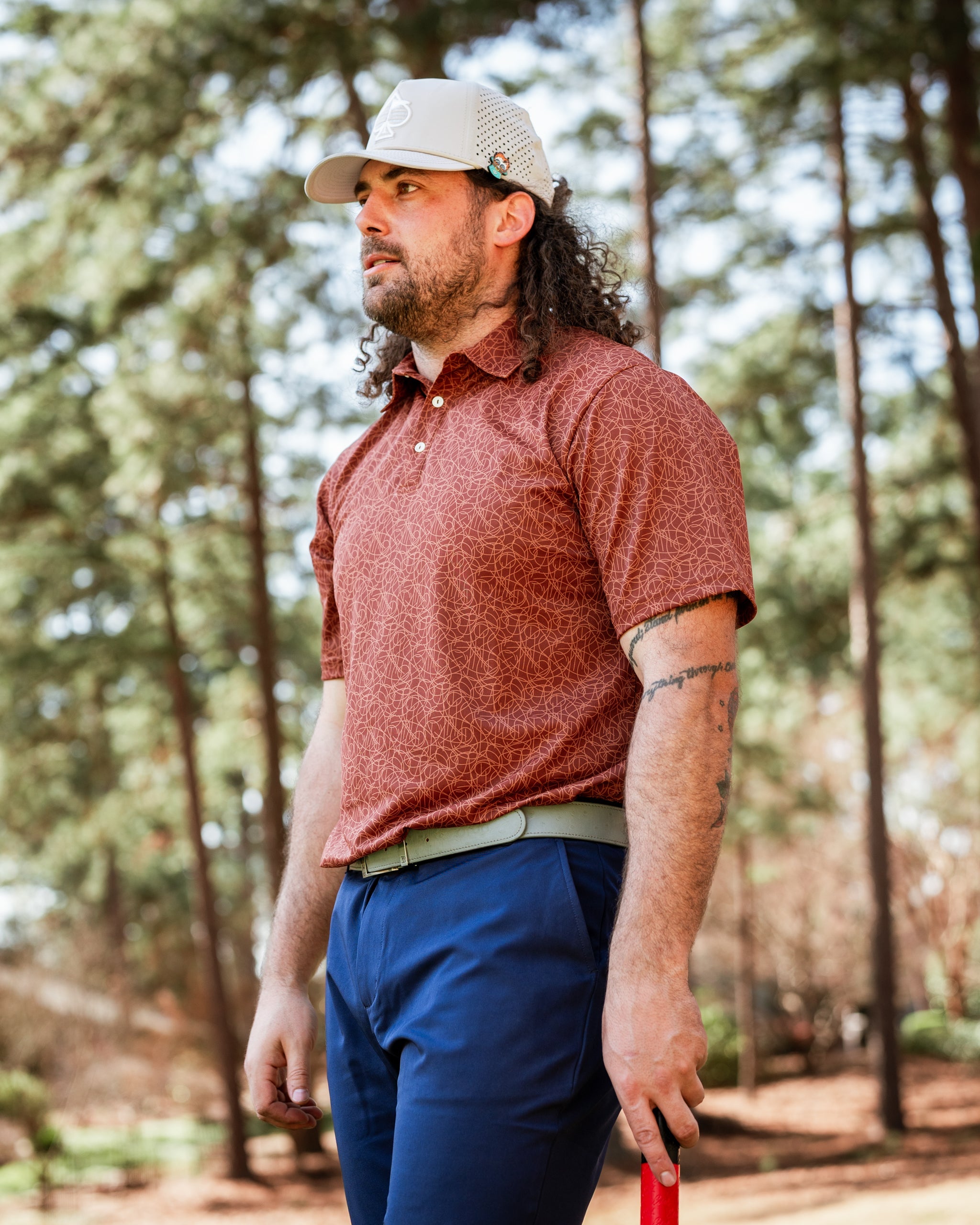 A golfer in a patterned rust polo shirt and navy pants stands confidently on the course, holding a putter.