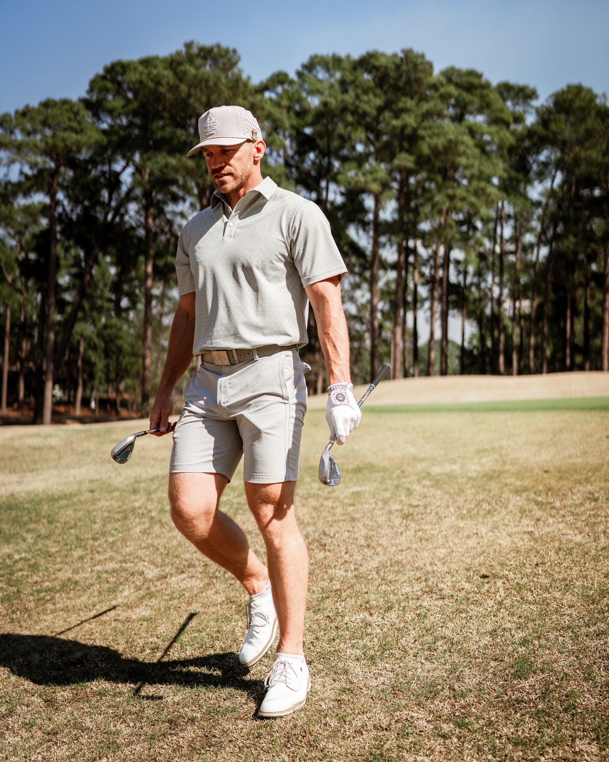 A golfer walks on the course wearing a light gray polo and shorts, showcasing a stylish and modern golf outfit.