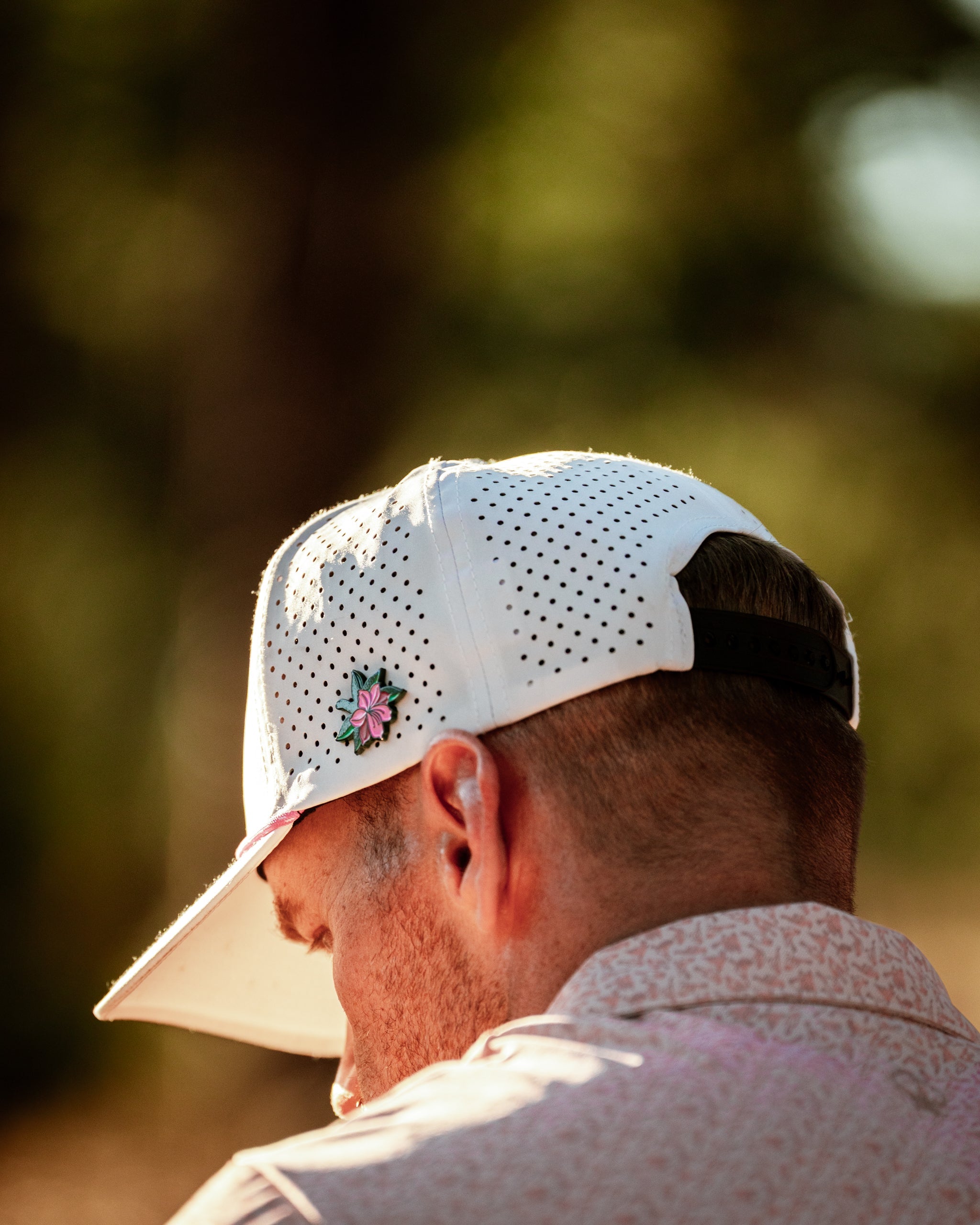 A man wearing a white perforated golf cap with a floral design, focused on the course in a natural setting.