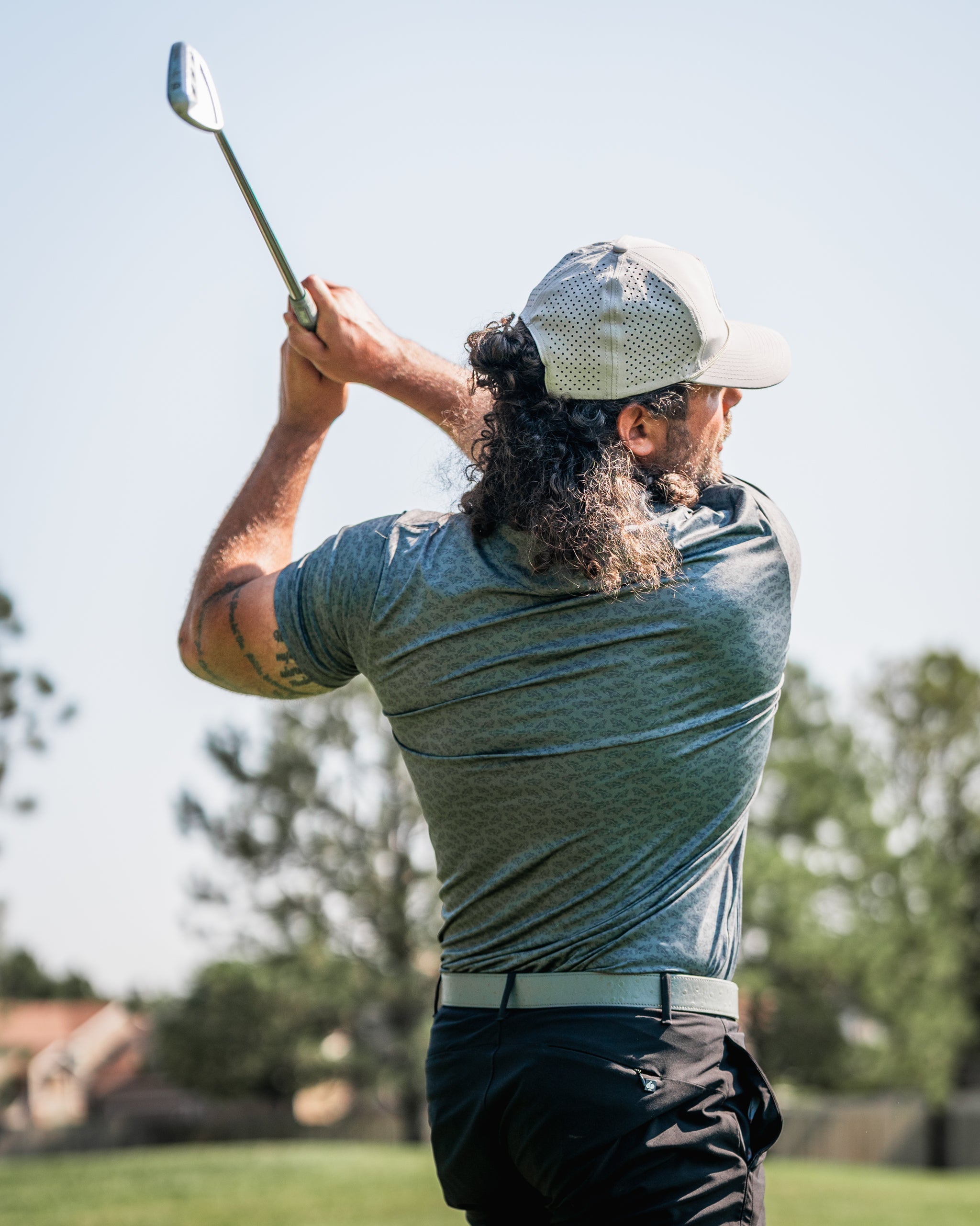 Golfer in a gray shirt and cap swings a club on a sunny day, showcasing a powerful backswing on the course.