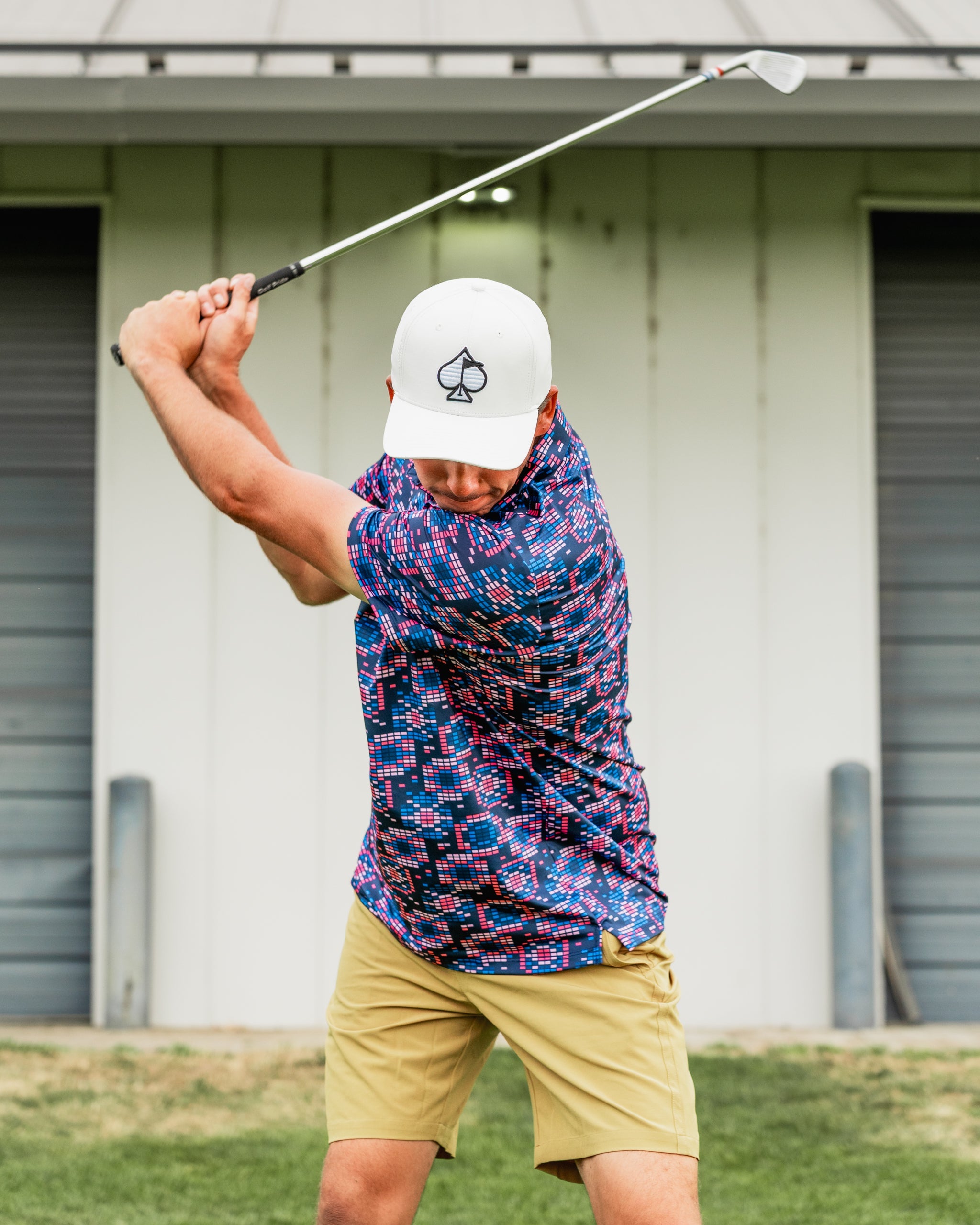 A golfer in a colorful Tetrafloral Dark shirt swings a club on the course, showcasing bold patterns and style.