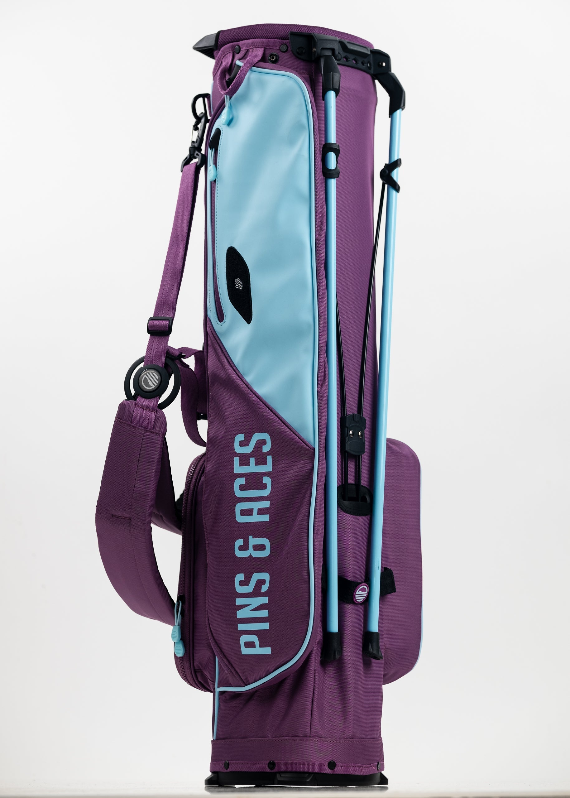 Bold purple golf bag with light blue accents, featuring PINS & ACES branding, golf clubs, and unique headcovers.