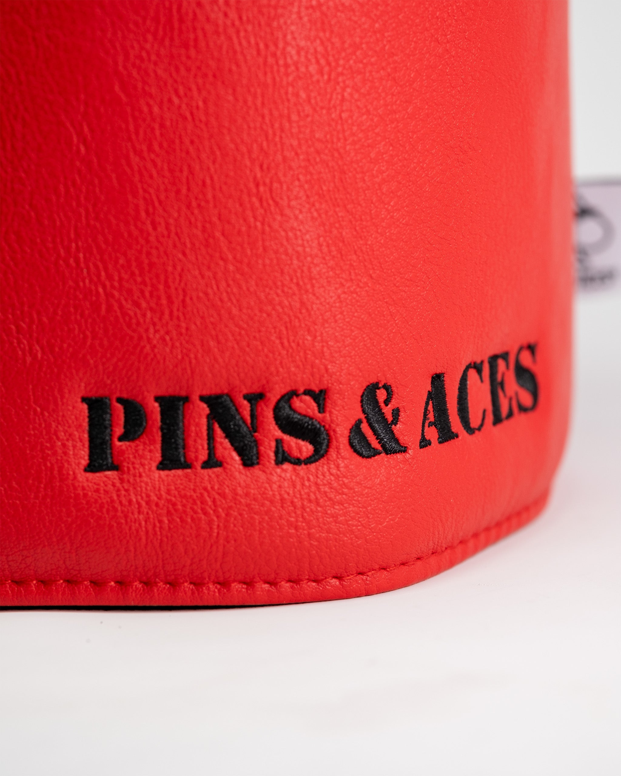 Close-up of a red driver cover with black embroidered text reading "PINS & ACES" on a white background.