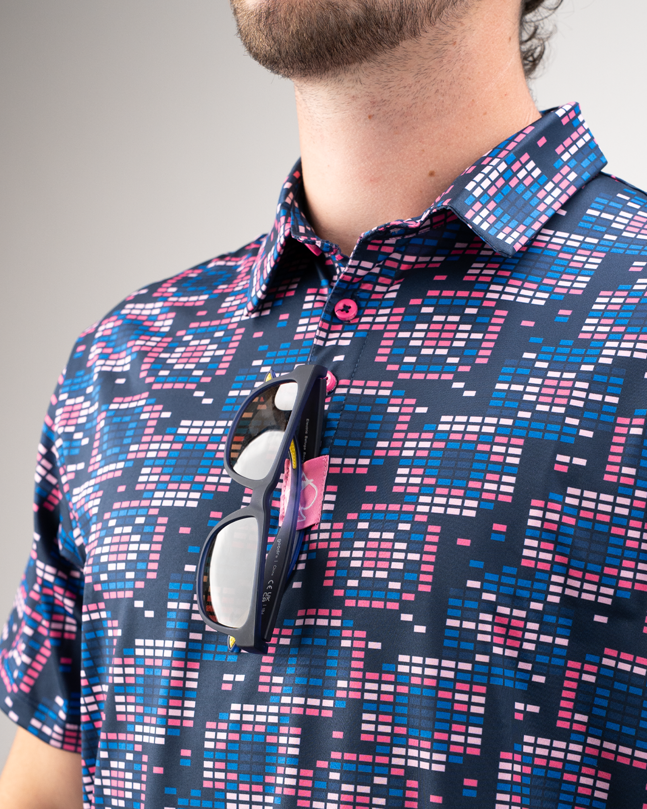 Men's Tetrafloral Dark golf shirt featuring a vibrant geometric pattern in navy, pink, and blue, with sunglasses resting on the collar.