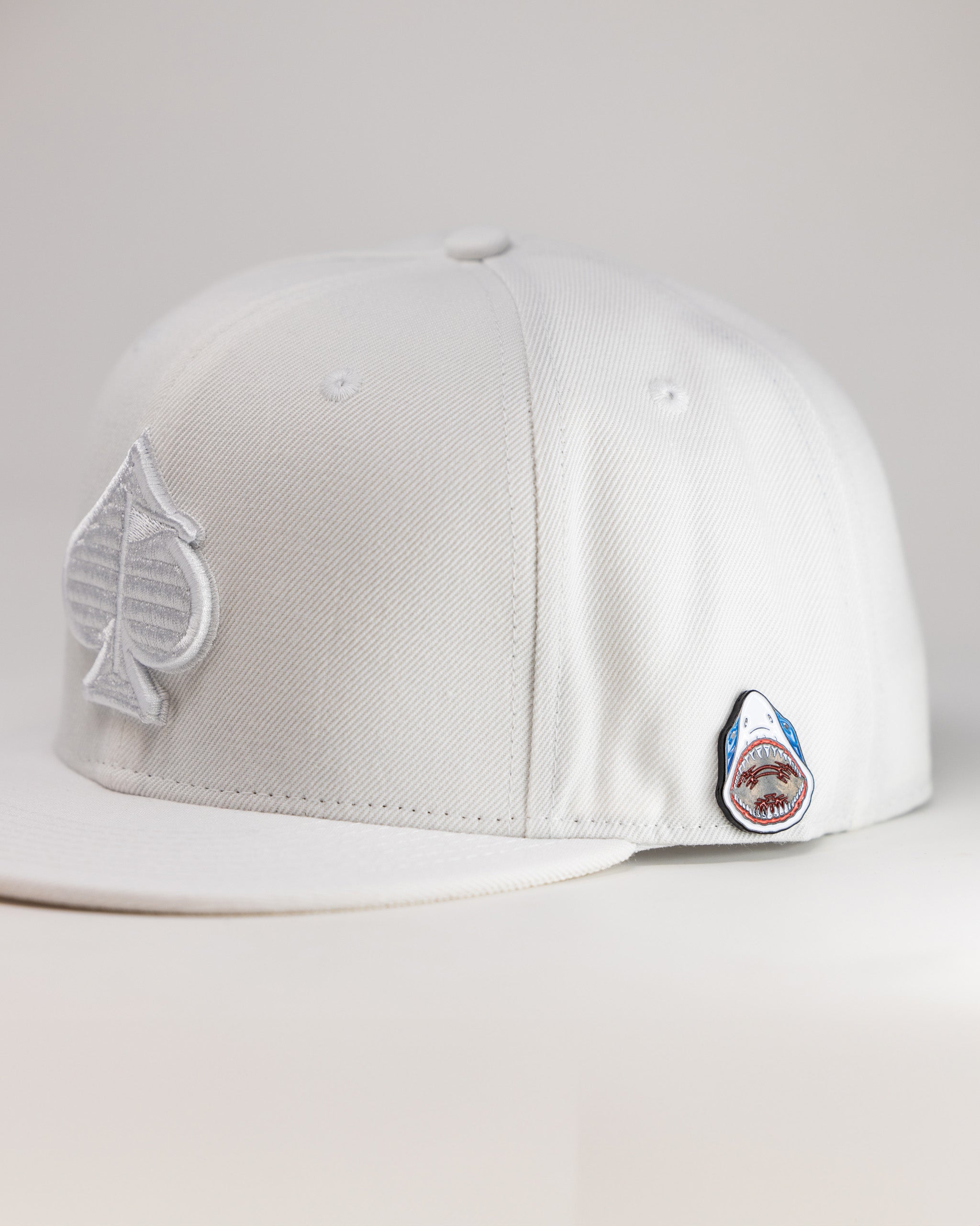 White golf cap with embroidered patches featuring a leaf and a shark, perfect for bold, unique golf style.