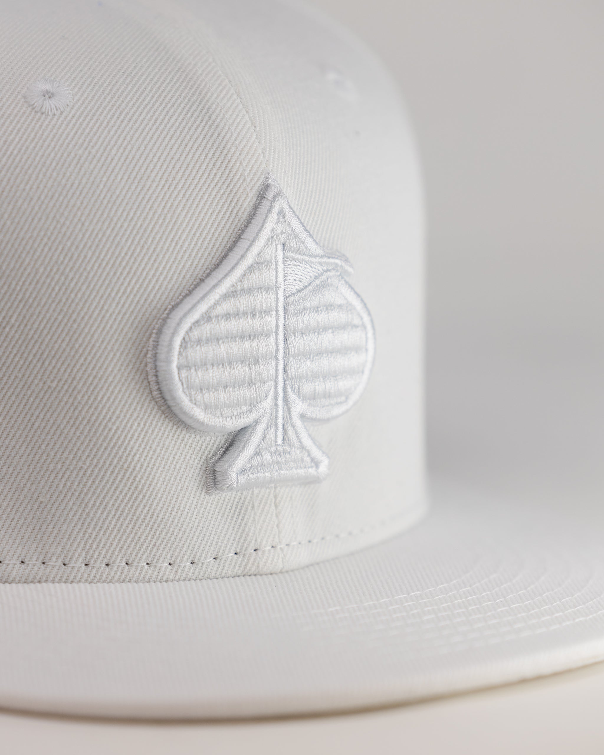 White golf cap with embroidered spade logo, bold and unique style for standout golfers on the course.