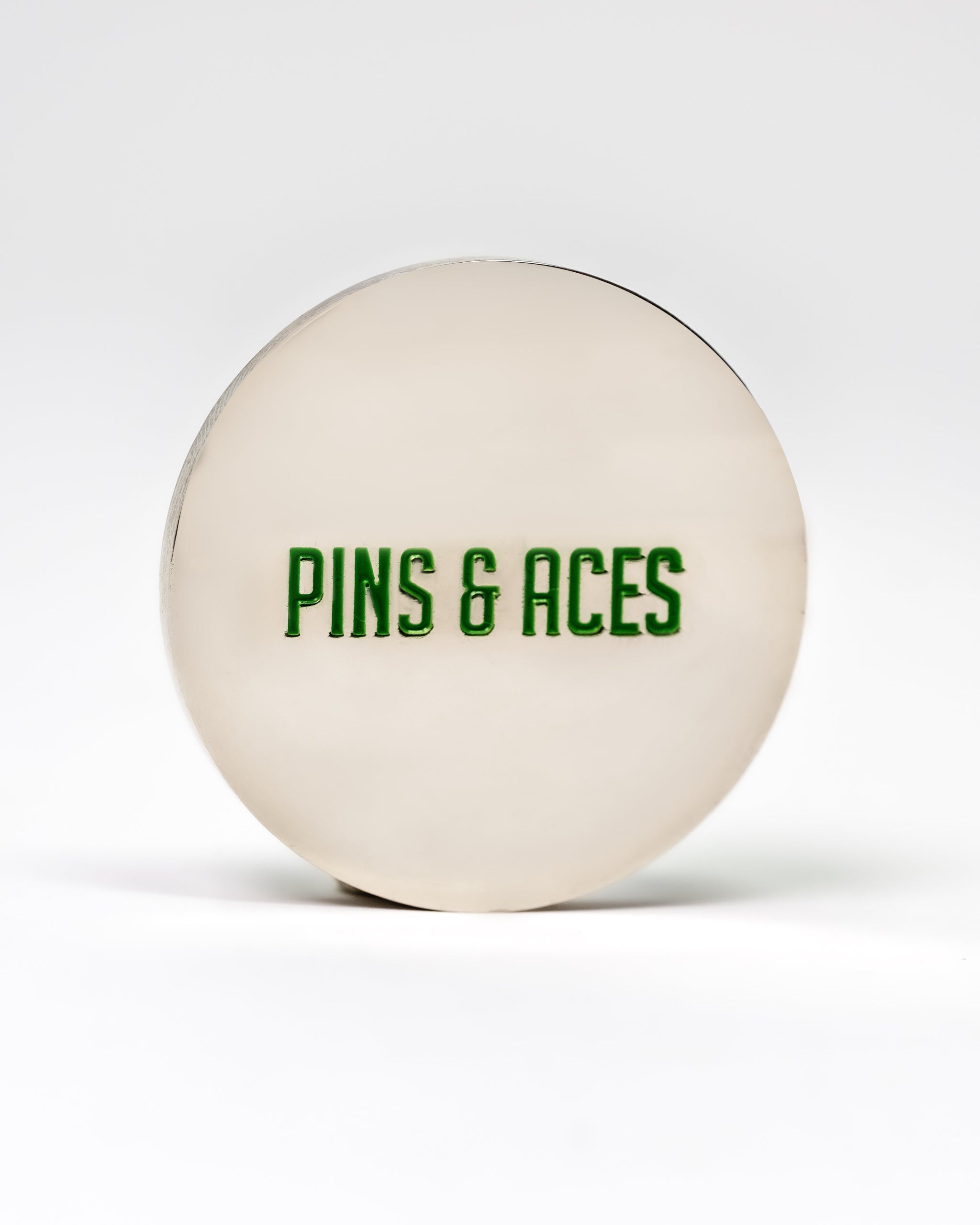 Alt text: "6 Milly - Wintergreen Ball Marker featuring a large, white, circular design with 'PINS & ACES' printed in green font centered on the surface."
